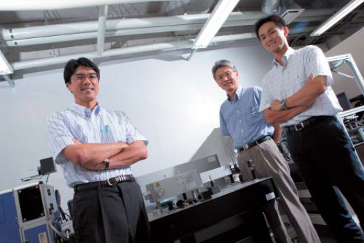 大阪大学構内に設置されたレーザー照射機と創晶のメンバー。左から森勇介代表取締役、高野和文顧問、安達宏昭代表取締役社長