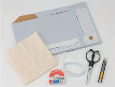 材料はA4サイズの書類ケース（本体）、布（蓋）、包装紙（装飾用）。ホームセンターなどで売っている塩化ビニール製のU字型パッキンをはめ込めばケーブル出し入れ用の穴の縁を保護できる