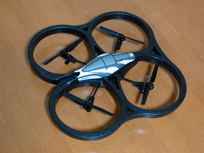 AR.Drone本体。ローター（プロペラ）ガードが付いた屋内用ハル（機体）を装着した状態。左側が前方。全長約52.5cm×幅約51.5cm、重さ420g。高さは実測で約11.5cm